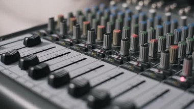Çok kanallı bir ses karıştırma konsolunun ön plan faders 'dan renkli EQ düğmelerine kadar bir rafa odaklı açılı yakın çekimi. Arka planda yanıp sönen gösterge ışıkları ve kanal şeritleri görünür.