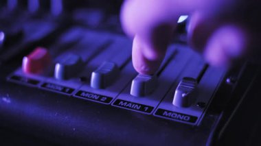 Profesyonel bir ses karıştırıcının ana ses kaydını yukarı iten bir parmağın aşırı yakın çekimi. Bir kırmızı efekt fader mavi renkten mor renge değişen dinamik renkli ışıklandırmayla görünür.