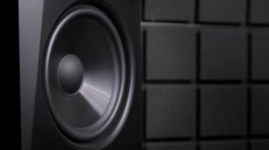 Yoğun bastan yavaş çekimde titreşen siyah bir hoparlörün yakın çekimi. Ses sürücüsü karanlık akustik panellerin arka planında ses dalgaları oluşturur.