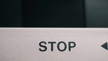 Klasik gümüş bir güvertede siyah desenli stop düğmesine basan bir parmağın makro yakın plan görüntüsü. Retro kontrol paneli açık kalın harfler ve bir ok içerir.