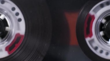 Destede çalan eski bir ses kasetinin makro yakın çekim görüntüsü. Kırmızı kalemli beyaz makaralar manyetik bant oynatıcının içinde açılırken sürekli dönüyor..