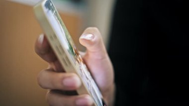 Düşük odaklı akıllı telefonu tutan bir kadının son derece yakından çekilmiş bir yan görüntüsü. Başparmağı karanlıkta aydınlatılmış ekranın içeriğinde hızla kayar..