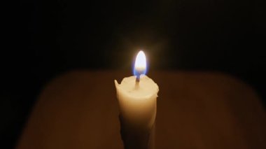 El, karanlık bir odada yanan bir kibritle tek bir mum fitili yakar. Alevler yanıp sönüyor, kamera uzaklaştığında siyah arka plana sıcak, yumuşak bir parıltı saçıyor..