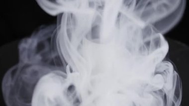 Tek kullanımlık elektronik sigara siyah arka plana kalın beyaz buhar salar. Dramatik stüdyo ışıklandırması yavaş çekimde dönen duman bulutlarını vurgular.