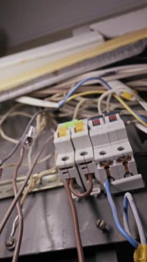 Beyaz devre kesiciler elektrik dağıtım panelinin içindeki karmaşık renkli bakır kablolara bağlanıyor. Kamera, metal kaplama içindeki kaotik kablo yönetimini ortaya çıkarıyor.