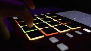 Müzisyen elleri, neon stüdyodaki aydınlatılmış MIDI pedlerine parmak vuruyor. Elektronik müzik üretimi, hip hop dayağı ve modern ses teknolojisi kavramı.