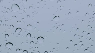 Statik yakın çekim, gri bir gökyüzüne karşı cam yüzeyde dinlenen su damlacıklarını yakalar. Huzur, melankolik, hava durumu ve huzurlu anlar kavramı..