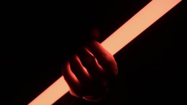 Bir insan eli parlayan kırmızı bir ışık tüpünü kavrayıp serbest bırakır ve zifiri karanlık bir ortamda dramatik gölgeler yaratır. Gelecekteki güç kavramı, cazibe ve bilim kurgu teknolojisi..