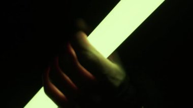 Bir el, parlak bir LED ışık tüpünü kavrayıp siyah bir arkaplana karşı canlı renklerde dolaşır. Fütürist teknoloji kavramı, gece hayatı atmosferi ve soyut yaratıcı aydınlatma..