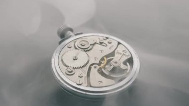 Eski bir gümüş cep saatinin iç mekanizması dişlileri ve yayları gösteriyor. Metal makinelerin üzerinden yoğun beyaz duman akıyor. Konsept, zamanın gizemli bir şekilde geçtiğini gösteriyor..