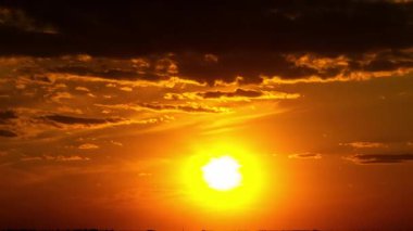 Karanlık bir ufukta batan parlak güneşin zamanı. Alevli turuncu ve kırmızı bulutlar, akşam alacakaranlığı sırasında canlı bir ışıltıya dönüşürken gökyüzünde sürükleniyor..