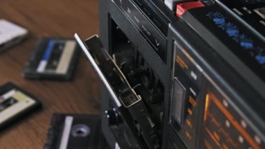 Bir el, ahşap bir masanın üzerindeki klasik bir teyp kayıt cihazına sarı bir ses kaseti yerleştirir. Retro müzik kültürü, analog teknoloji nostaljisi ve 1980 'lerin yaşam tarzı kavramı..