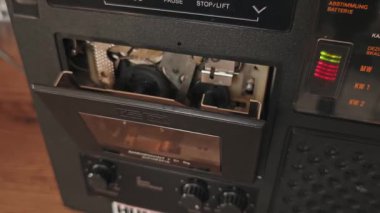 Bir el şeffaf bir kaseti klasik bir çalar güvertesine yerleştirir ve mekanik kapıyı kapatır. Görünür iç makaralı temiz kabuk ses aygıtının endüstriyel tasarımını vurgular.