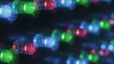 Panelde yanıp sönen renkli LED ışıklarının makro yan görüntüsü. Kırmızı, yeşil ve mavi diyotlar sığ bir alan derinliğiyle ortaya çıkarak canlı, teknolojik ve soyut bir arkaplan oluştururlar..