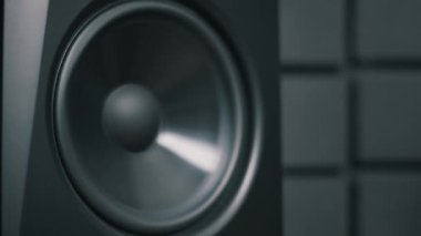 Dolly siyahi bir hoparlörden uzaklaşarak profesyonel bir stüdyo monitörünü gösterdi. Yüksek kaliteli ses ekipmanları koyu renkli akustik köpük duvarda duruyor..