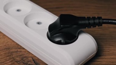 Siyah zemin kapsülünü kavrayan bir erkek elin yakın plan çekimi ve onu beyaz bir üçlü eklenti bloğundan çekiyor. Koyu renk bir tahta masadaki eylem bir aygıtın bağlantısını kesiyor..