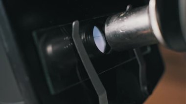 Eski bir mikroskobun odak noktasını ayarlayan bir elin açılı yakın çekimi. Metal objektif mercek, laboratuvar araştırmaları için cam bir slaytta insan saçı örneği inceliyor..