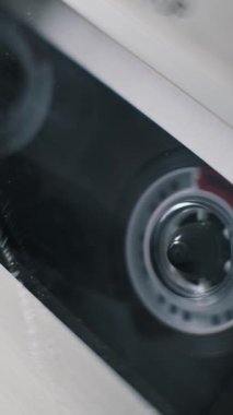Şeffaf bir ses kasetinin Hollanda açılı makro görüntüsü çalarken dönüyor. Bu mobil video, hareket halindeki klasik analog ortam teknolojisini yakalar.