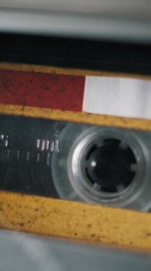 Eski, yıpranmış sarı ve kırmızı ses kasetlerinin dikey bir videosu. Kayıt makarası bandın şeffaf penceresindeki zaman işaretçilerini göstermek için döner.