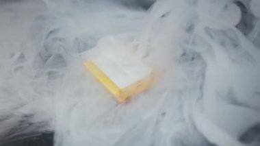 Lityum polimer batarya batarya hücresi karanlık bir yüzey üzerinde yatar ve duman çıkarmaya başlar. Kalın beyaz buhar dalgalanır ve tehlikeli güç kaynağını sarar..