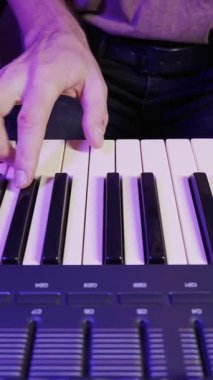 Erkek eller bir sentezleyicinin siyah ve beyaz tuşlarında bir melodi çalar. Sahne parlak mor ışıkla aydınlanıyor, yaratıcı ve karamsar bir atmosfer yaratıyor..