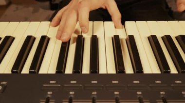 Müzisyenin elleri bir kayıt stüdyosundaki bir MIDI sentezleyici klavyesinde bir melodi çalar. Yakın çekim, siyah ve beyaz tuşlar arasındaki sıcak ışıklandırmayla parmak hareketlerine odaklanır.