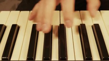 Erkek eller dijital piyano klavyesinde hem siyah hem de beyaz tuşlara basarak müzikal bir parça çalar. Yakın çekim, yukarıdan aşağı görüntü performansı sıcak, yumuşak ışıklandırmada yakalar.