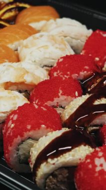 Somon ve kırmızı tobiko da dahil olmak üzere çeşitli suşi dürümleri siyah servis tepsisine yerleştirilmiş. Kara unagi sosu, parlak stüdyo ışıkları altında susam tohumlarının üzerinde parlıyor..