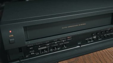 Erkek el, siyah VHS kaseti motorlu VCR oynatıcıya yerleştirir. Yakın çekim mekanik ve retro-90 'ların ev eğlencesi teknolojisini ön plana çıkarıyor.