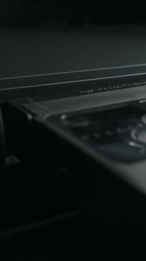 Siyah bir VHS kaseti antika bir VCR oynatıcıya takan bir elin yakın plan görüntüsü. Nostalji kavramı, retro teknoloji, ev filmleri izlemek ve analog medya tarihi.