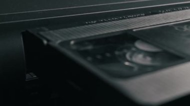 Siyah bir VHS video kaseti eski bir VCR oynatıcıya yerleştirip kaseti yükleyen bir elin yakın çekimi. Retro teknoloji kavramı, nostalji, 80 'ler, 90' lar ve modası geçmiş medya.