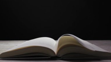 Ahşap masa üzerine açık bir kitap. Sayfalar rüzgârda karanlık arka planda hızla dönüyor. Sihir, gizem, hikaye anlatma ve bilgi edinme kavramı.