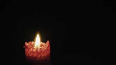 Bal peteği desenli kırmızı bir balmumu, izole edilmiş siyah bir arkaplana karşı titreşen bir alevle yanar. Anma, maneviyat, meditasyon ve sükunet kavramı.