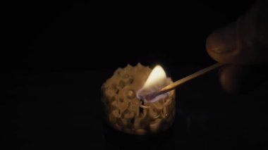 Kibriti olan bir el siyah arka planda dekoratif bir bal peteği bal mumu yakar. Umut, maneviyat ve barış kavramı..