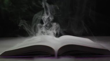 Karanlık bir arka planda açık bir büyü kitabı büyüleyici bir ışıltıyla gizemli mor bir duman yayar. Yasak bilgi kavramı, kara büyü, fantezi edebiyatı ve antik sırlar..
