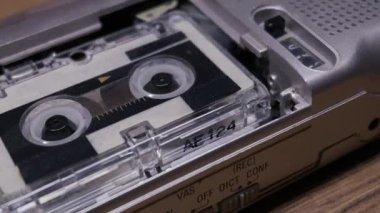Gümüş renkli bir mikrokaset kaydedici ahşap bir masada çalışır ve bant içinde çalışır. Retro gazetecilik, casusluk teknolojisi ve analog ses geçmişi kavramı.
