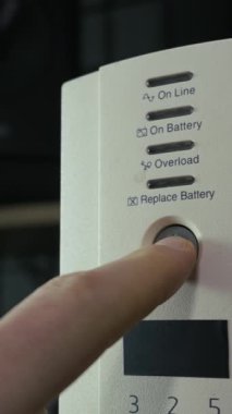 Bir erkek parmak, beyaz kesintisiz güç ünitesinin güç düğmesine basarak onu çalıştırır. Elektrik güvenliği kavramı, yedek enerji çözümleri ve veri koruma teknolojisi.