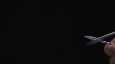 Bir adamın eli, küçük metal bir tırnak makasını tutar ve onu koyu bir arka plana yaslar. Bakım, titiz bakım, hassasiyet ya da bir göreve hazırlık kavramı.