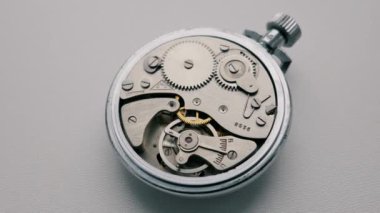 Yakın çekim, hareket eden vitesli eski bir gümüş kronometrenin karmaşık iç mekanizmasına yakınlaşır. Zaman yönetimi kavramı, teslim tarihi baskısı ve klasik mühendislik.