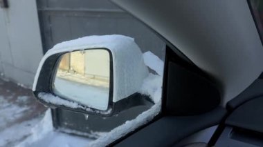 Kalın kar ve buzla kaplı yan aynayı gösteren bir arabanın içinden bak. Otomatik kanat aynası pencereye doğru içe doğru katlanır. Kavram, kış sürüş zorluklarını gösteriyor.