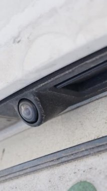 Beyaz bir aracın kirli tamponundaki tozlu bir kamera lensinin makro görüntüsü detaylıdır. Otomotiv teknolojisi, sürüş güvenliği ve kirli kış yolu kirliliği kavramı.