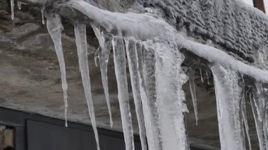 Dondurucu kış havasında beton çatı kenarından sarkan kalın, berrak buz sarkıtları. Aşırı soğuk, mevsimsel iklim değişiklikleri ve tehlikeli dondurucu hava tehlikeleri kavramı.