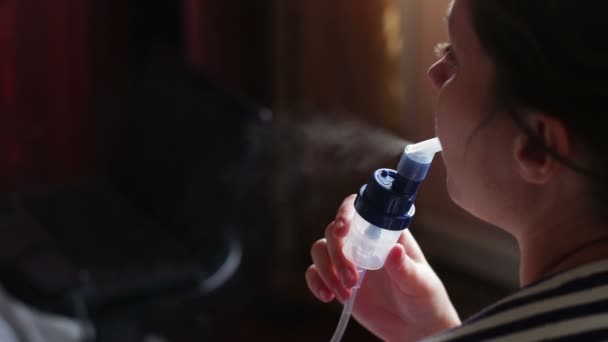 Woman wears a mask for inhalation, and conducts the procedure lungs inhalation using a nebuliser. — Stockvideo