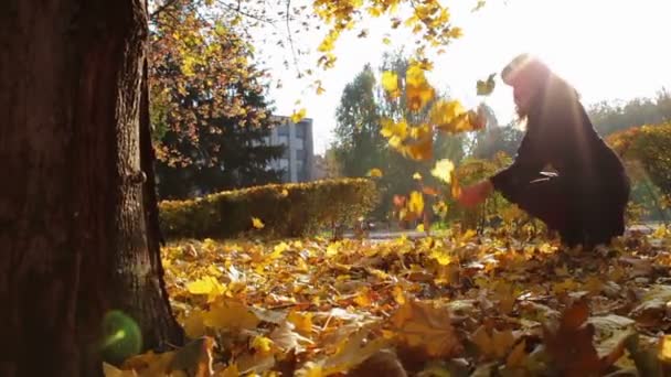 Une fille jette des feuilles jaunes des branches d'arbres dans le parc d'automne .