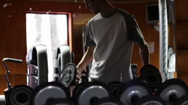 Der Mann im Fitnessstudio schüttelt seinen Bizeps mit Gewichten. — Stockvideo