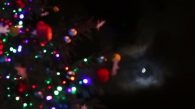Ay'ın arka planında geceleri oyuncaklar ve ışıklarla süslenmiş Noel ağacı.