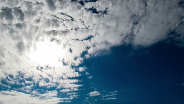 Wolken bewegen sich am blauen Himmel auf dem Hintergrund der strahlenden Sonne. — Stockvideo