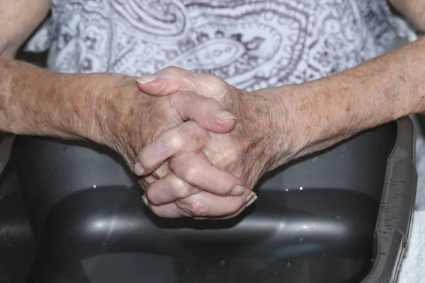 The hands of a senior lady washing her hands above a bowl of water.