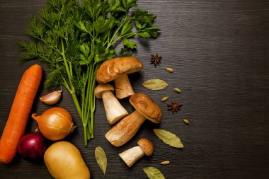 Sebzeler, otlar ve baharatlarla kaplı karanlık bir arka planda beyaz orman mantarları. Tahta masadaki taze mantarlar..