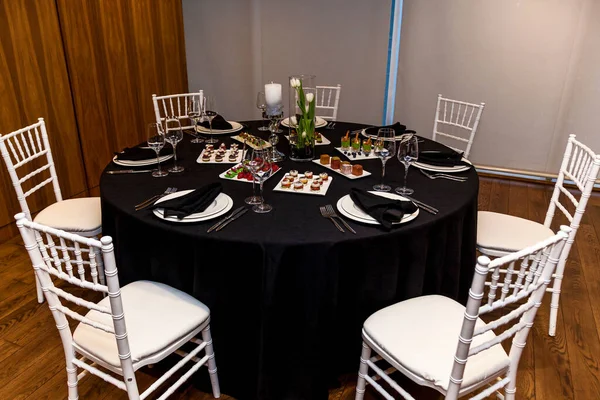 Round table with black tablecloth and black napkins, set of cutlery with snacks for the banquet. Catering, server tables for bonquet